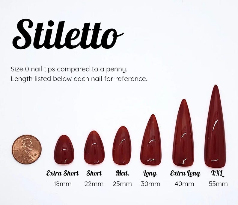Puede incluir: Un conjunto de seis puntas de u&ntilde;a stiletto de color rojo oscuro en longitudes variables de 18mm a 55mm, etiquetadas Extra Short, Short, Med., Long, Extra Long y XXL. Se muestra un centavo de cobre para escala. El texto dice Stiletto.