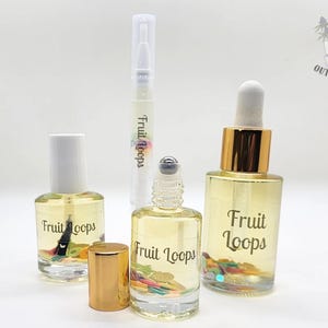May include: A collection of clear glass bottles filled with a yellow liquid and colorful confetti. The bottles include a nail oil, a rollerball bottle, a dropper bottle, and a pen-style applicator. The text "Fruit Loops" is printed on the bottles.