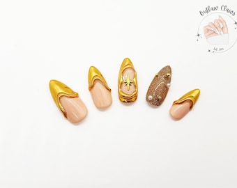 Puede incluir: Cinco uñas postizas doradas y con purpurina con base nude. Las uñas presentan una variedad de diseños, incluyendo una estrella, un remolino y purpurina.