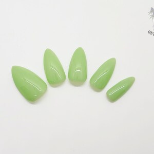 May include: Five almond-shaped, light green press-on nails arranged on a white surface. The nails have a glossy finish. The Outlaw Claws logo is in the upper right corner.