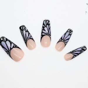 May include: Five long, nude-colored fake nails with a black and white butterfly design on the tips. The design features a gradient of purple and white.