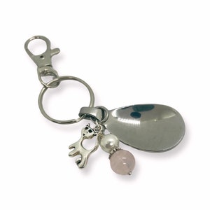Może przedstawiać: Srebrny brelok do kluczy z zawieszką w kształcie łyżki, małym zawieszką w kształcie kota, białą perłą i różową perłą z różowego kwarcu.