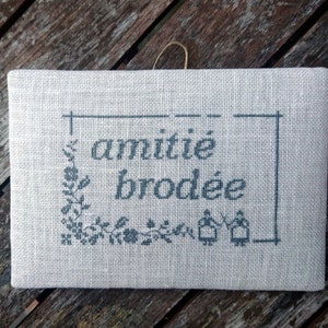 May include: A beige linen fabric with a black embroidered design that says "amitié brodée".