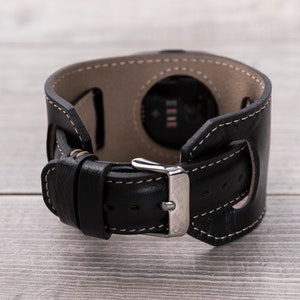 May include: Black leather watch band with a silver buckle and a cut-out for the watch face.