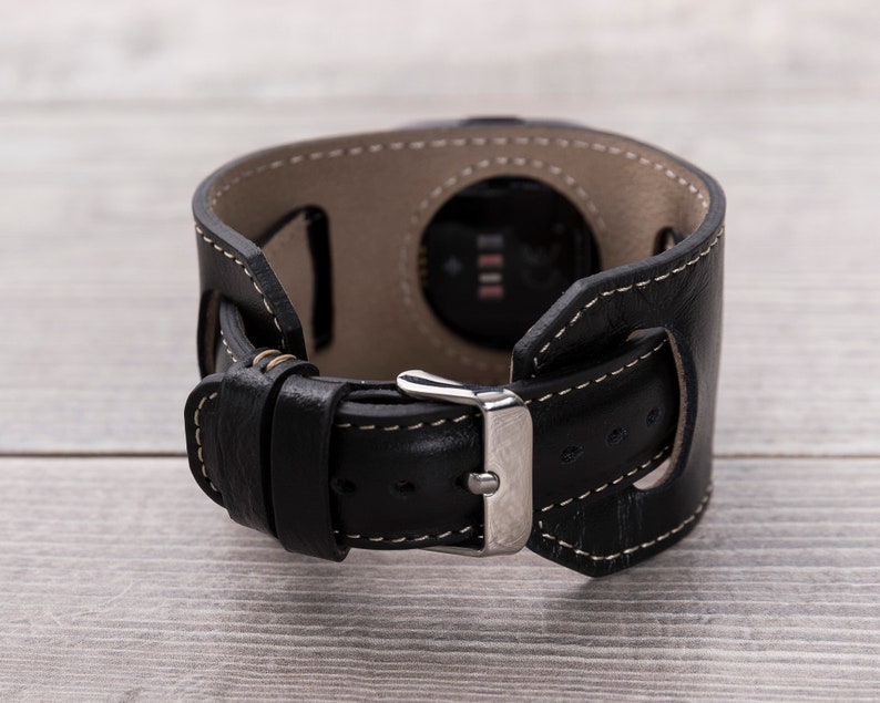 May include: Black leather watch band with a silver buckle and a cut-out for the watch face.