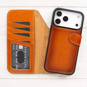 May include: A brown leather phone case with a wallet design. The case has slots for cards and a snap closure. A phone with a black case is attached to the wallet. The wallet is open, revealing the card slots and a clear window for a card.