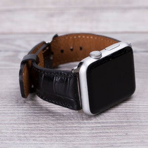 May include: A silver Apple Watch with a black leather strap. The strap has a crocodile pattern.