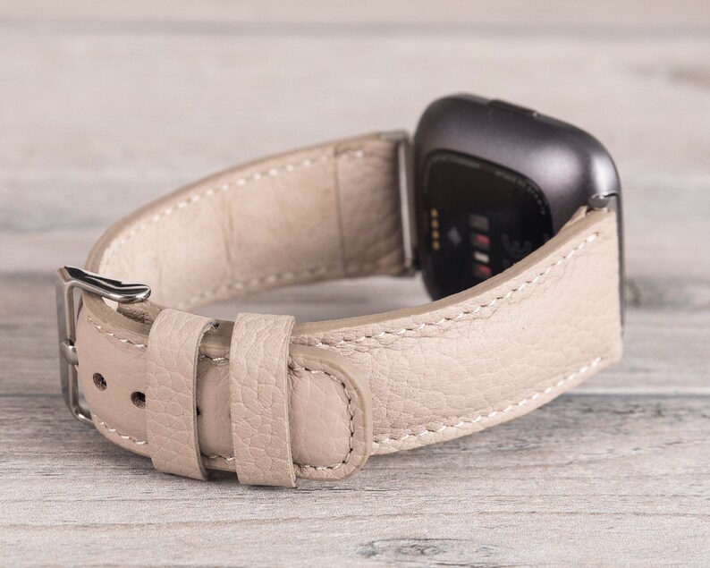 Puede incluir: Una correa de reloj de cuero beige con una hebilla plateada. La correa est&aacute; dise&ntilde;ada para un reloj inteligente con una cara cuadrada.