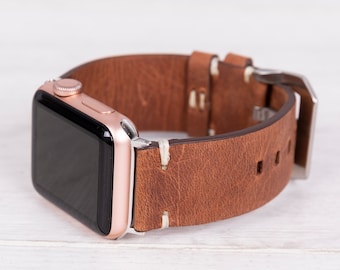 May include: A rose gold Apple Watch with a brown leather band. The band has white stitching and a silver buckle.