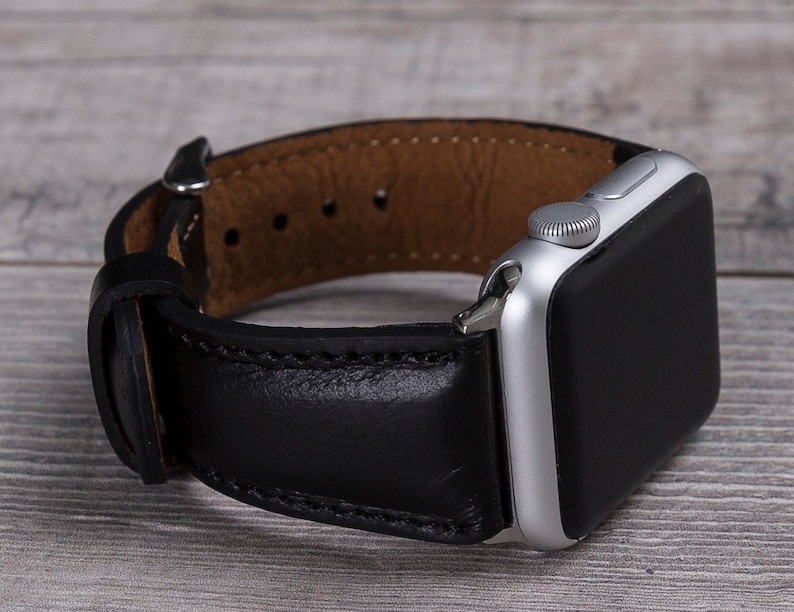Black leather Apple Watch band with stainless steel buckle displayed on a flat surface.