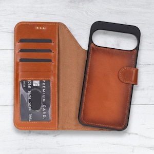May include: A brown leather phone case with a wallet design. The case has slots for cards and a clear window for an ID. The phone case is open, revealing the interior and a black phone holder.