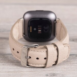 Puede incluir: Una correa de reloj de cuero beige con una hebilla plateada. La correa est&aacute; dise&ntilde;ada para un reloj inteligente con una pantalla negra.