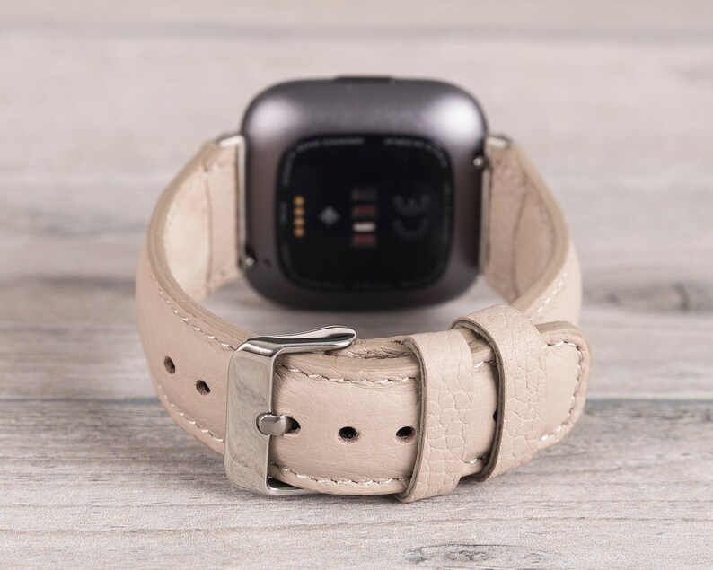Puede incluir: Una correa de reloj de cuero beige con una hebilla plateada. La correa est&aacute; dise&ntilde;ada para un reloj inteligente con una pantalla negra.