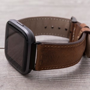 Puede incluir: Un reloj inteligente negro con una correa de cuero marr&oacute;n. La esfera del reloj es de forma cuadrada con una pantalla negra.