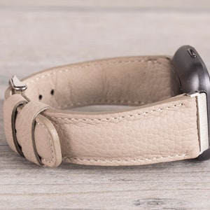 Puede incluir: Una correa de reloj de cuero beige con una hebilla plateada. La correa est&aacute; dise&ntilde;ada para un reloj inteligente de forma cuadrada.