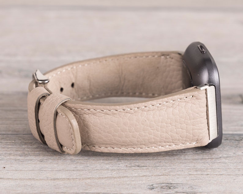 Puede incluir: Una correa de reloj de cuero beige con una hebilla plateada. La correa est&aacute; dise&ntilde;ada para un reloj inteligente de forma cuadrada.