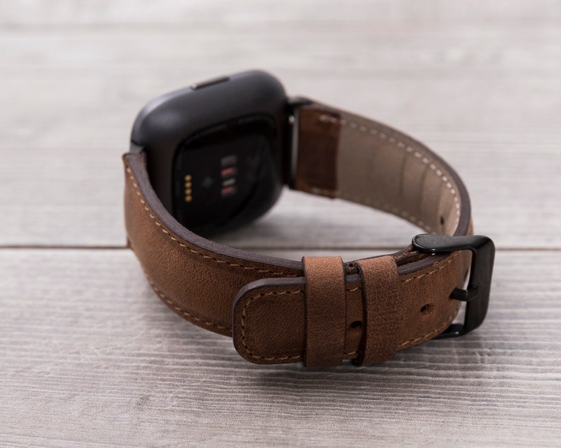 Puede incluir: Una correa de reloj de cuero marr&oacute;n con una hebilla negra. La correa est&aacute; dise&ntilde;ada para un reloj inteligente de forma cuadrada.