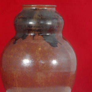 May include: A brown ceramic vase with a dark brown glaze. The vase has a rounded body and a wide mouth.