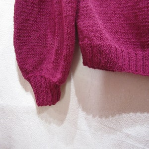 May include: A close-up of a pink knitted sweater with long sleeves and a ribbed hem.