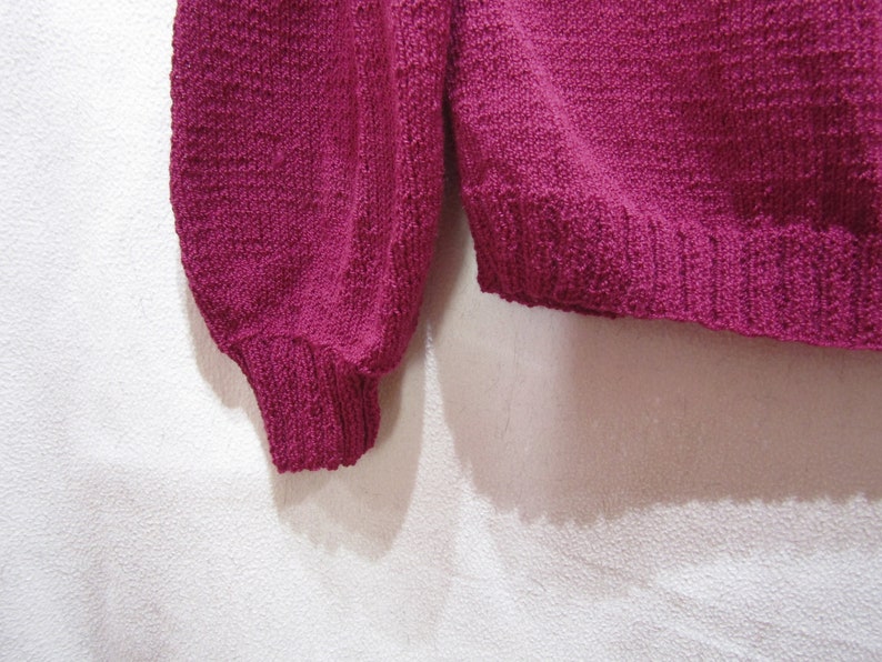 May include: A close-up of a pink knitted sweater with long sleeves and a ribbed hem.