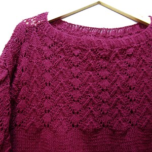 May include: A deep burgundy knitted sweater with a delicate openwork pattern. The sweater has a round neckline and long sleeves.