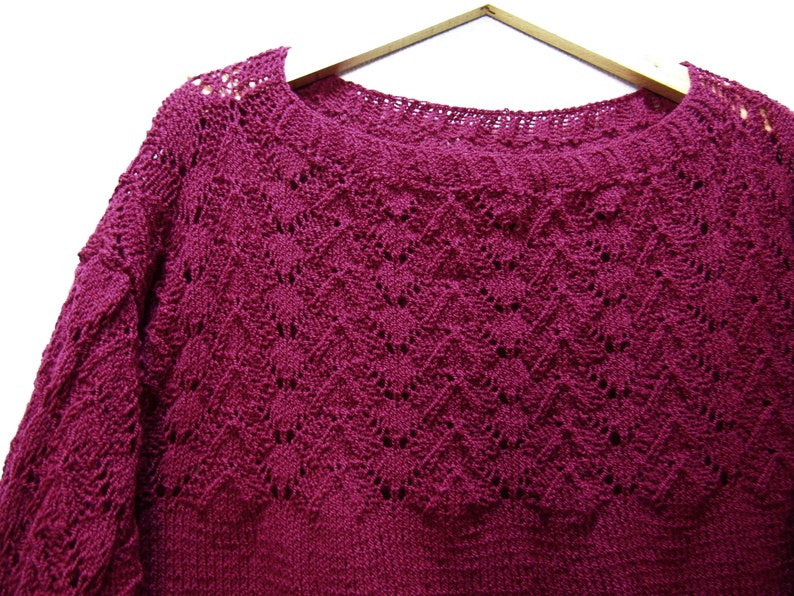 May include: A deep burgundy knitted sweater with a delicate openwork pattern. The sweater has a round neckline and long sleeves.