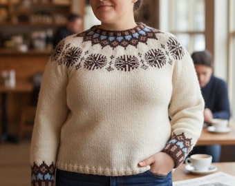 Pode incluir: Camisola creme com gola e punhos estampados. A gola apresenta um design repetitivo em castanho e azul, com punhos a condizer. A camisola é combinada com calças de ganga azuis. A pessoa está num café.