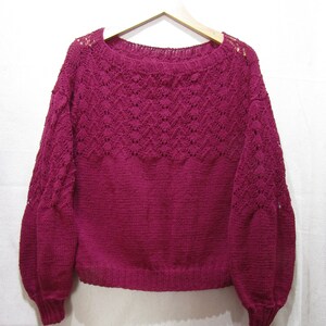 May include: A deep burgundy knitted sweater with a lacy pattern around the neckline and sleeves.