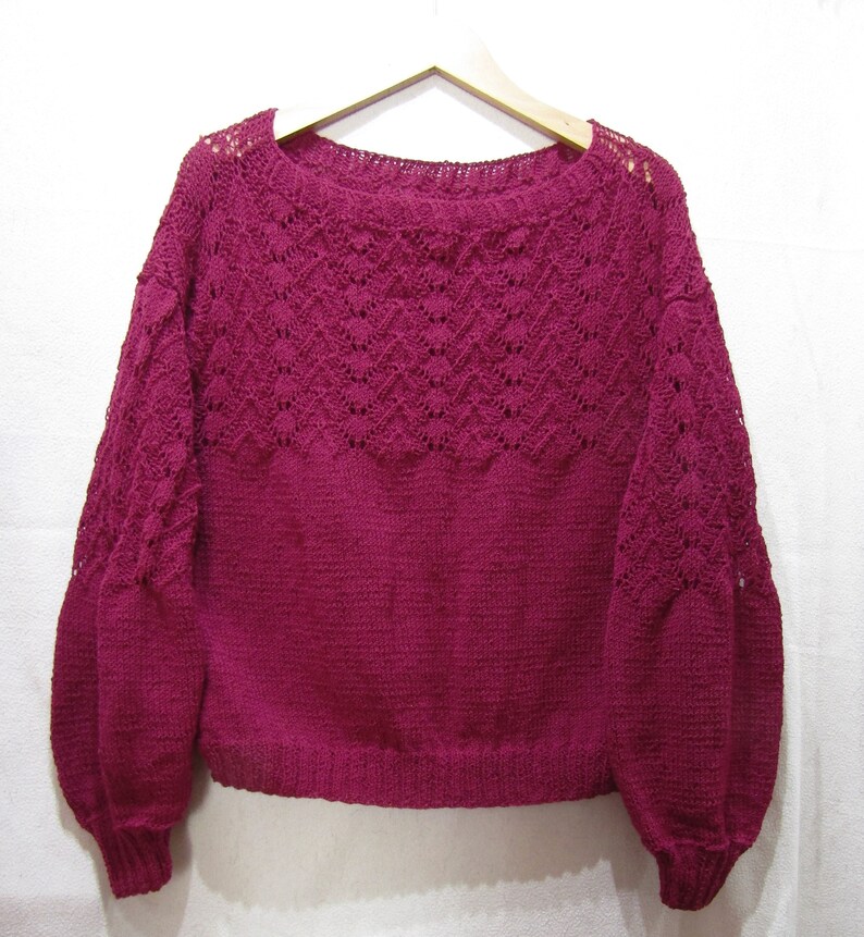 May include: A deep burgundy knitted sweater with a lacy pattern around the neckline and sleeves.
