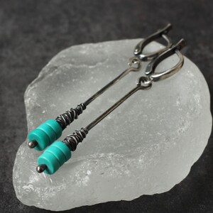 Può includere: Lunghi orecchini in argento con perline turchesi. Gli orecchini hanno un design delicato con una sezione avvolta in filo e una chiusura a gancio. Le perline turchesi sono di un colore vivace, aggiungendo colore.