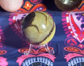 May include: A polished sphere of banded agate with brown and yellow stripes. The sphere is displayed on a clear plastic stand.