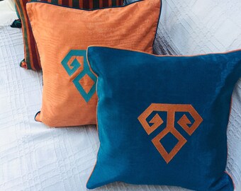 May include: Four decorative throw pillows in various colors. One is dark green, another has vertical stripes of red, orange, and green. Two are orange and teal, each with an embroidered geometric design. All have contrasting piping.
