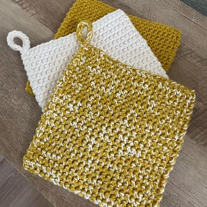May include: Three crocheted pot holders in yellow and white. The pot holders are stacked on top of each other. The top pot holder is yellow and white, the middle pot holder is white, and the bottom pot holder is yellow.