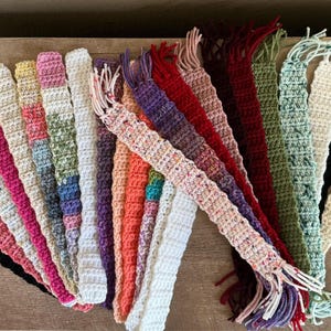 May include: A collection of colorful crocheted bookmarks with fringe. The bookmarks are made with different colored yarns and have a variety of patterns.