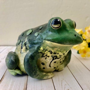 May include: A hand-painted ceramic frog figurine with green and yellow paint. The frog has a textured surface and a realistic appearance.