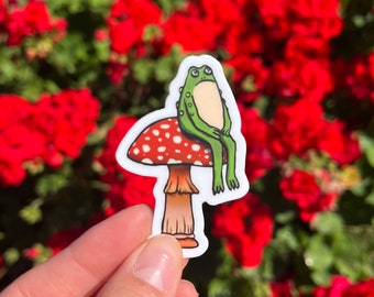 Vinyl Weatherproof Cute Cottage Toad on Red Mushroom Nature Sticker | Quirky Grumpy Woodland Green Garden Frog Sitting on Stool Chair Decal