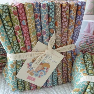 Puede incluir: Paquetes de tela floral en varios colores, incluyendo azul, rosa y verde, atados con cinta. Una etiqueta con el texto "Tilda flowers" está adjunta. La tela es parte de la "Quilt Collection".