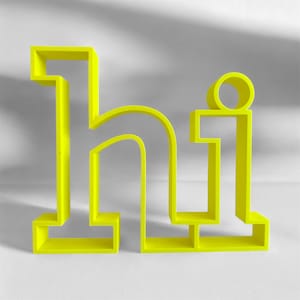 Könnte beinhalten: Eine leuchtend gelbe Skulptur des Wortes "hi". Die Buchstaben sind blockartig und modern, mit einem minimalistischen Design. Die Skulptur steht vor einem schlichten weißen Hintergrund.