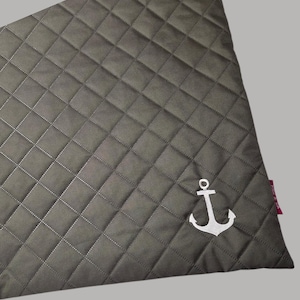 May include: A gray quilted fabric with a diamond pattern and white stitching. A white anchor emblem is embroidered in the lower right corner. The fabric has a tag on the right side.