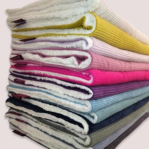 May include: A stack of 10 plush blankets in various colors, including white, yellow, pink, red, purple, blue, and green. Each blanket has a soft, fuzzy texture on one side and a corduroy texture on the other side.