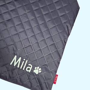 May include: Dark gray quilted pet blanket with the name "Mila" in light green script and a paw print. The blanket has a diamond pattern and a red tag with text.
