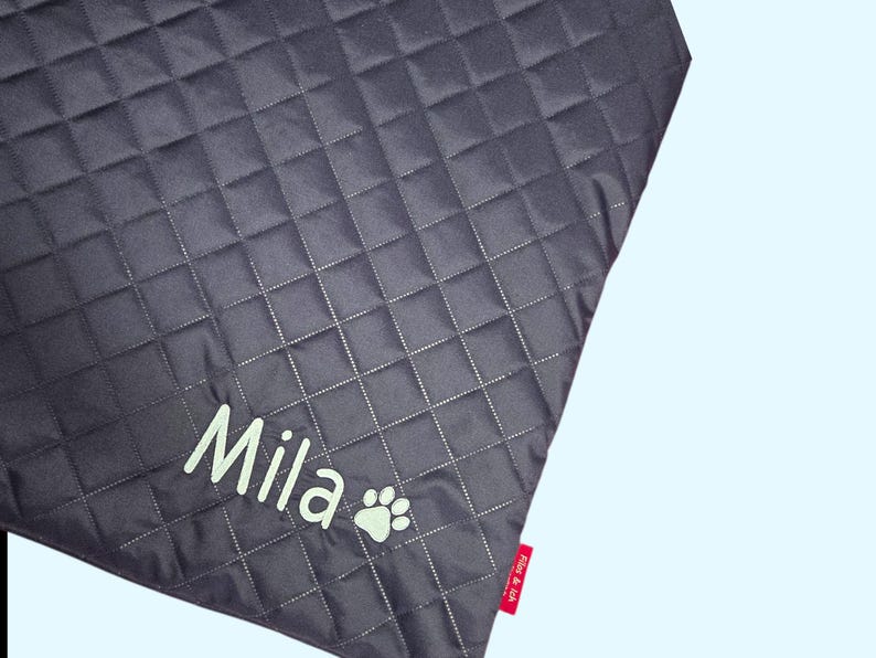 May include: Dark gray quilted pet blanket with the name "Mila" in light green script and a paw print. The blanket has a diamond pattern and a red tag with text.