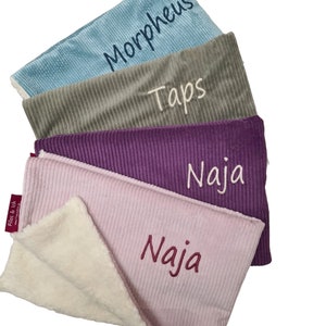 May include: Four personalized baby blankets in different colors and textures. The blankets are stacked on top of each other, with the top blanket folded in half. The blankets are made of a soft, plush material and have the names "Morpheus", "Taps", "Naja", and "Naja" embroidered on them.