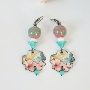 May include: A pair of dangle earrings with a floral design. The earrings feature a pink and green striped bead, a white bead, a turquoise bead, and a floral charm.