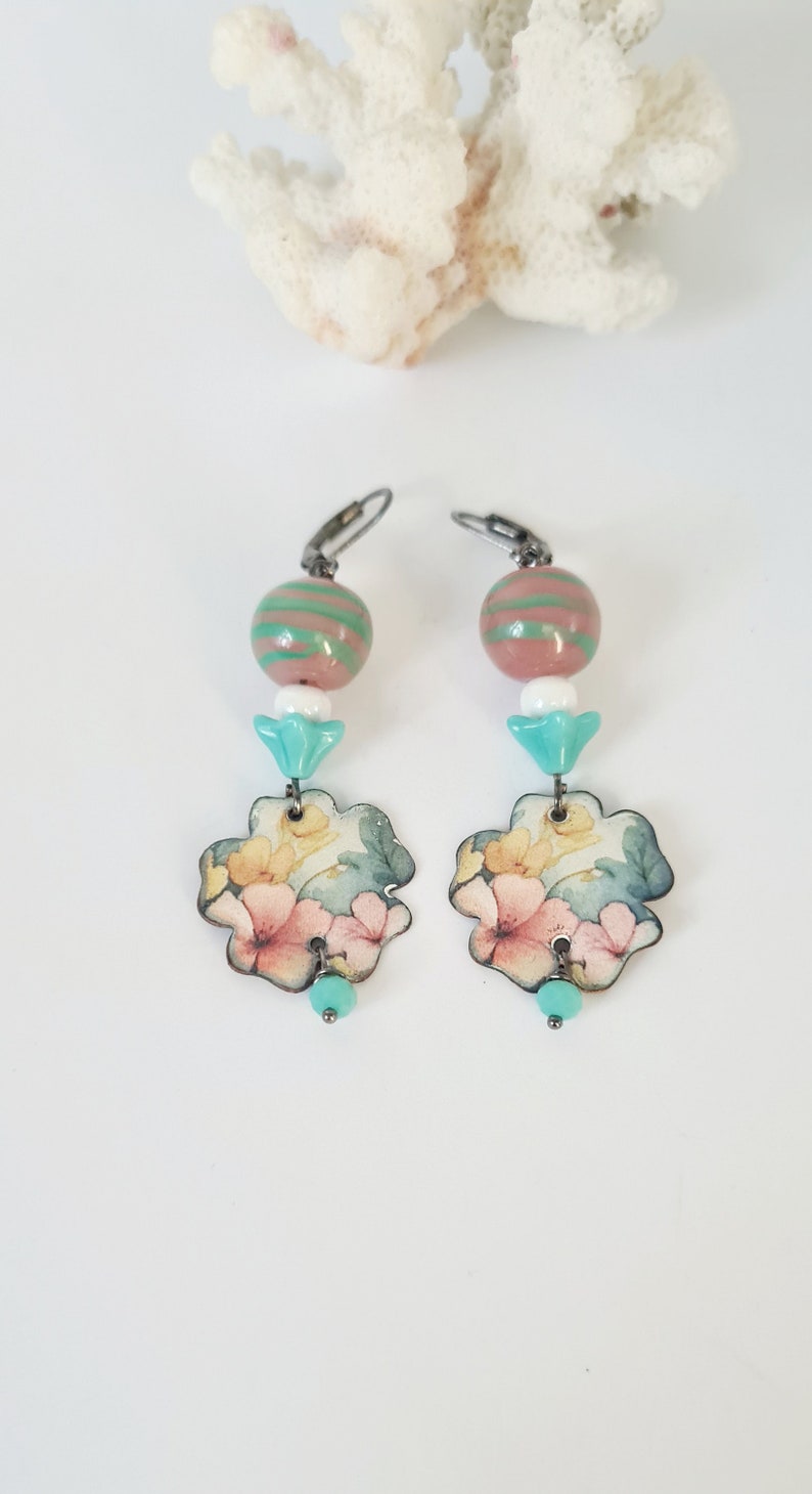 May include: A pair of dangle earrings with a floral design. The earrings feature a pink and green striped bead, a white bead, a turquoise bead, and a floral charm.