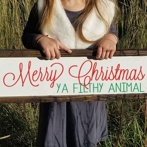 May include: A white wooden sign with a brown frame. The sign says "Merry Christmas Ya Filthy Animal" in red and green lettering.