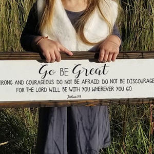 May include: A wooden sign with white paint and black lettering. The sign reads "Go BE Great" and includes a bible verse from Joshua 1:9. "Be strong and courageous. Do not be afraid; do not be discouraged, for the Lord will be with you wherever you go."