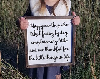 May include: A framed wooden sign with the quote "Happy are they who take life day by day, complain very little and are thankful for the little things in life" in black script on a white background. The frame is a dark brown color.