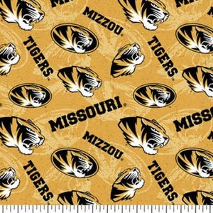 Peut inclure: Tissu dor&eacute; avec un motif r&eacute;p&eacute;t&eacute; de t&ecirc;tes de tigre noires et dor&eacute;es, les mots "Tigers", "Missouri" et "Mizzou". Le tissu a une r&egrave;gle en bas avec des mesures en pouces.