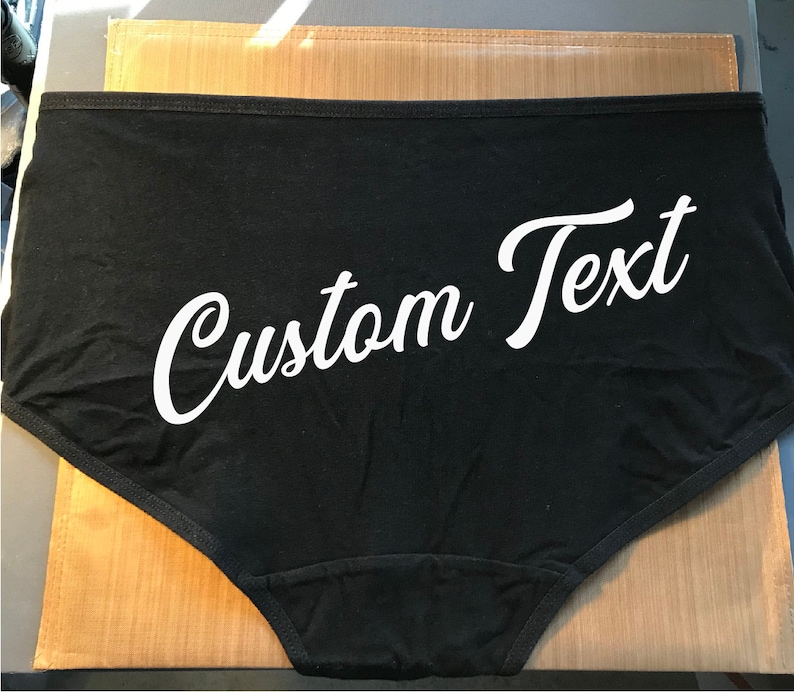 Pu&ograve; includere: Intimo in cotone nero con testo bianco che dice "Custom Text" in un carattere corsivo.